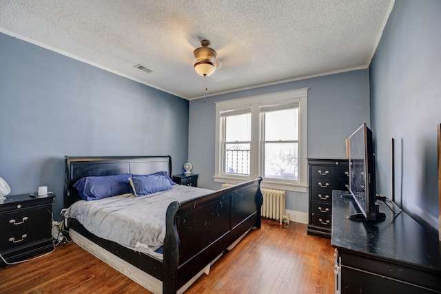 bedroom with visible vents, wood-type flooring, ornamental molding, and radiator heating unit