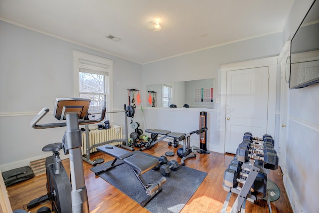 exercise room featuring visible vents, wood finished floors, radiator heating unit, crown molding, and baseboards