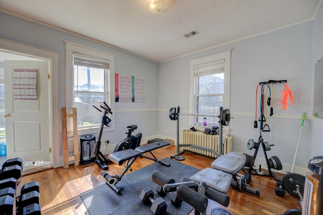 exercise area featuring ornamental molding, radiator, and wood finished floors