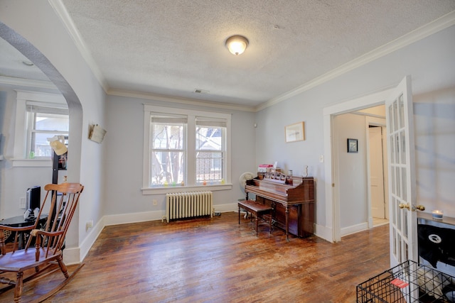 interior space featuring wood finished floors, baseboards, radiator heating unit, arched walkways, and ornamental molding