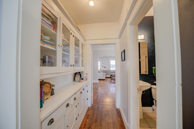 corridor featuring dark wood finished floors, baseboards, and arched walkways