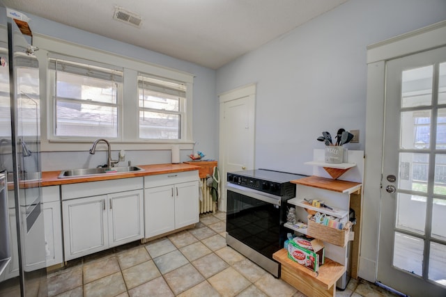 kitchen featuring visible vents, butcher block countertops, electric range oven, white cabinetry, and a sink