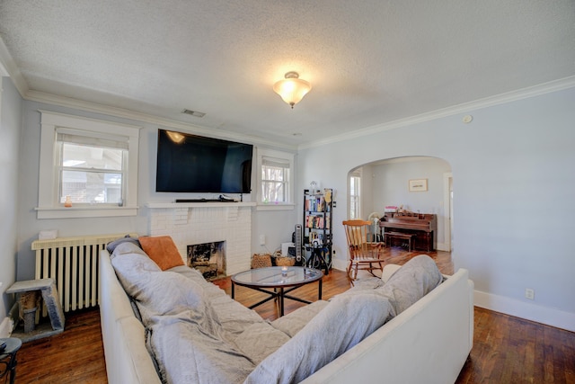 living room featuring a brick fireplace, radiator heating unit, wood finished floors, arched walkways, and a textured ceiling