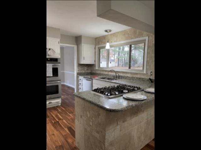 kitchen with dark wood-type flooring, a sink, stainless steel appliances, a peninsula, and white cabinets