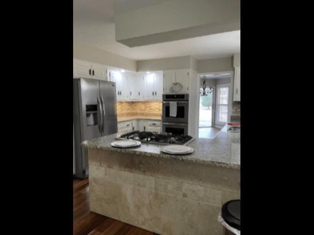 kitchen featuring tasteful backsplash, dark wood finished floors, appliances with stainless steel finishes, a peninsula, and white cabinets