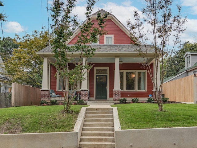 view of front of house with fence, roof with shingles, covered porch, a front lawn, and brick siding