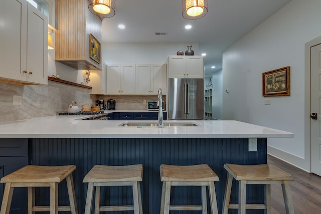 kitchen with a peninsula, a sink, light countertops, high quality fridge, and backsplash