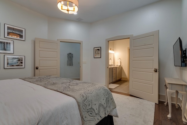 bedroom with wood finished floors, visible vents, ensuite bathroom, and baseboards