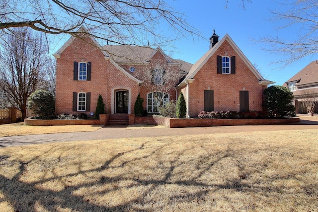 view of front of home featuring brick siding, a chimney, and a front yard