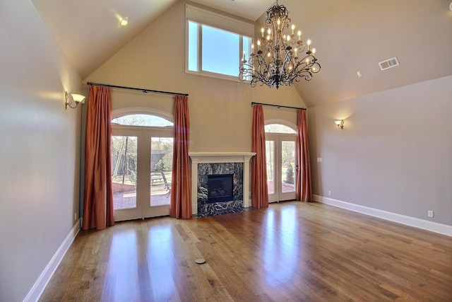 unfurnished living room featuring visible vents, high vaulted ceiling, wood finished floors, a high end fireplace, and baseboards