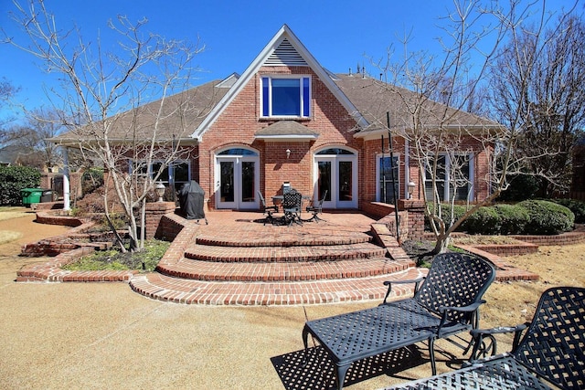 rear view of house with a patio, french doors, brick siding, and roof with shingles