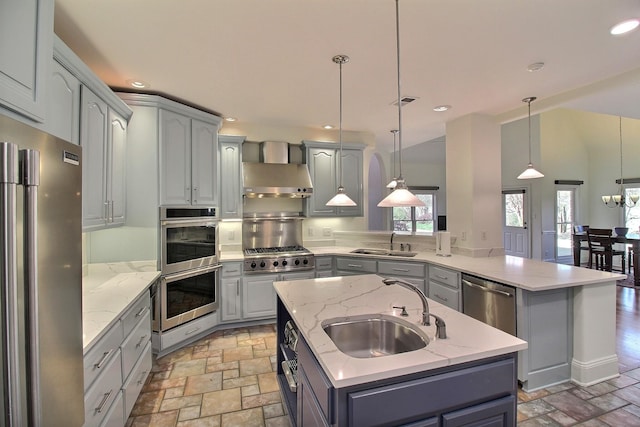 kitchen with a sink, stainless steel appliances, stone tile floors, and wall chimney range hood