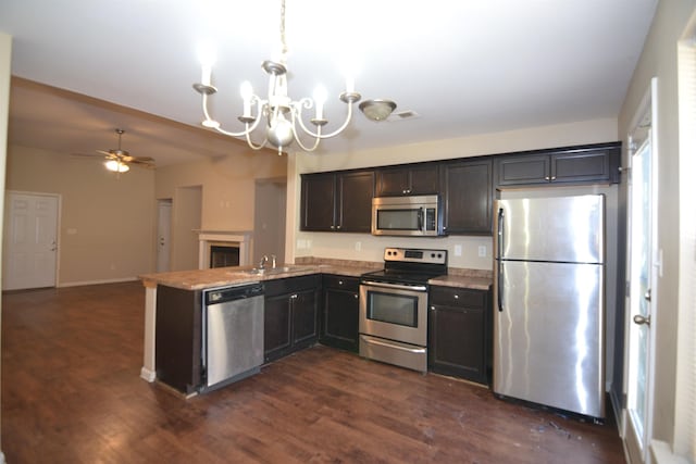 kitchen with a sink, dark wood-style floors, stainless steel appliances, a peninsula, and baseboards