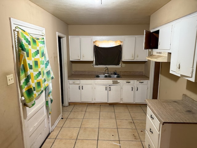 kitchen with a textured ceiling, white cabinets, light tile patterned flooring, and a sink