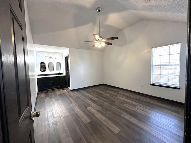 unfurnished bedroom with a textured ceiling, baseboards, ceiling fan, dark wood-style flooring, and vaulted ceiling