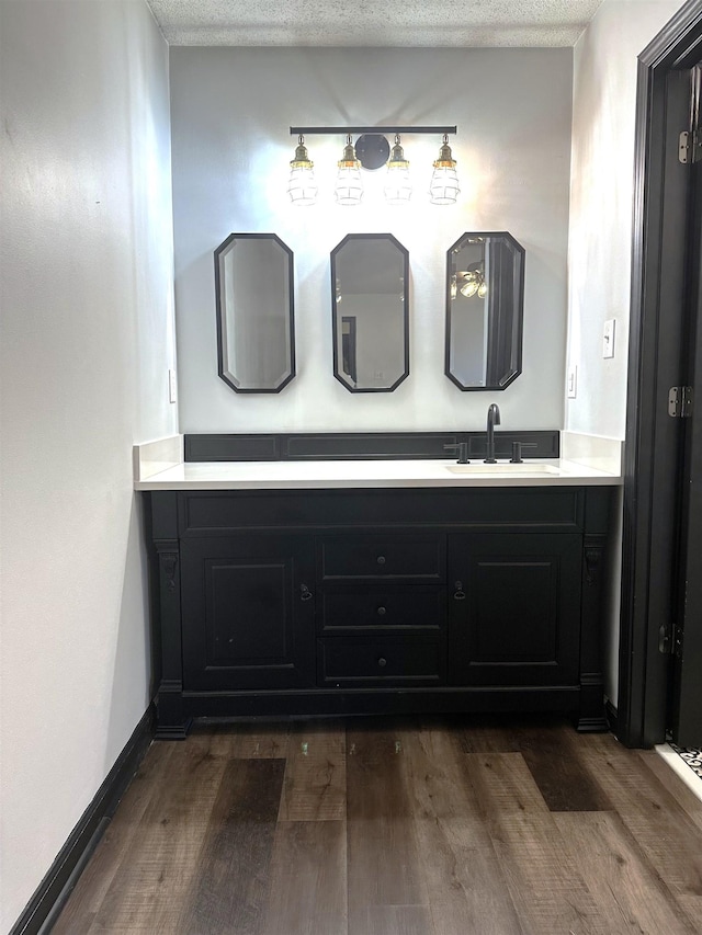 bathroom with baseboards, a textured ceiling, wood finished floors, and vanity