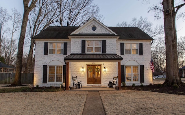 view of front facade featuring french doors, brick siding, a standing seam roof, and fence