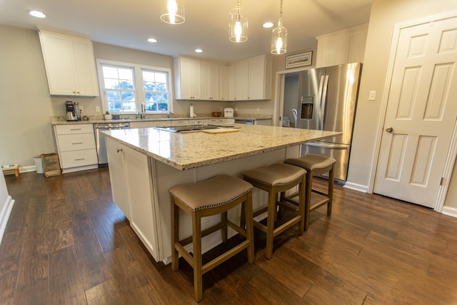 kitchen featuring light stone counters, dark wood-style floors, stainless steel appliances, white cabinetry, and a center island