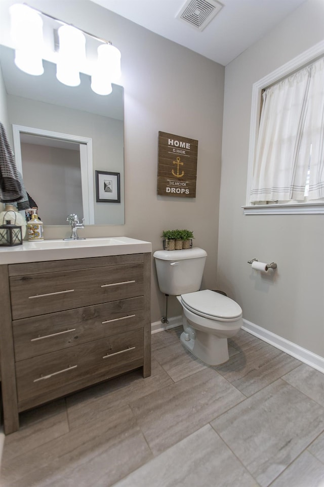 half bath with visible vents, toilet, vanity, and baseboards