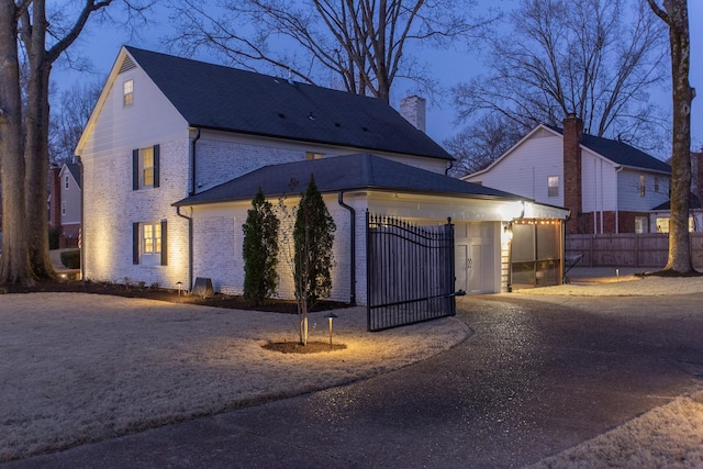 exterior space featuring a gate, fence, driveway, an attached garage, and brick siding