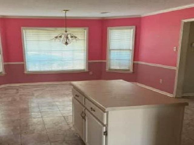 kitchen with hanging light fixtures, white cabinets, a kitchen island, and ornamental molding