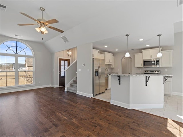 kitchen featuring visible vents, a breakfast bar, open floor plan, appliances with stainless steel finishes, and light stone countertops