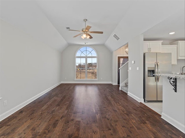 unfurnished living room with baseboards, visible vents, ceiling fan, dark wood-type flooring, and vaulted ceiling