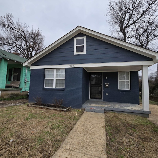 bungalow with brick siding, covered porch, and a front yard