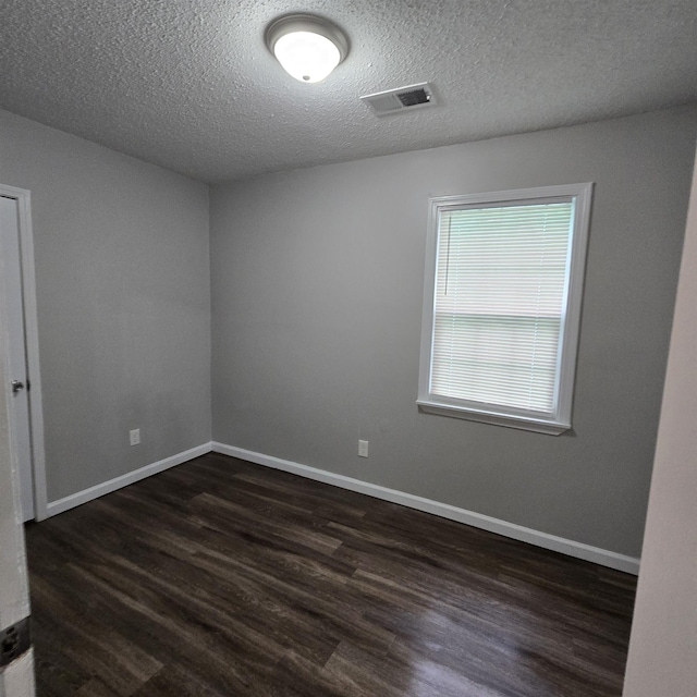 spare room featuring visible vents, baseboards, a textured ceiling, and dark wood-style floors