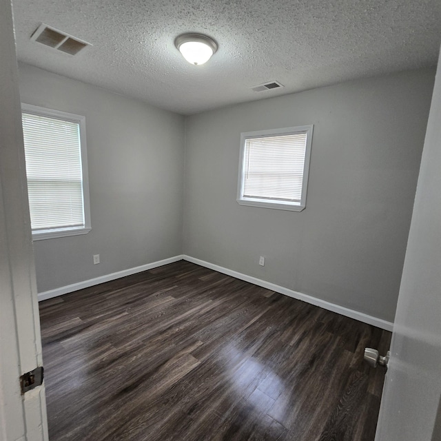 unfurnished room featuring visible vents, baseboards, dark wood-type flooring, and a textured ceiling