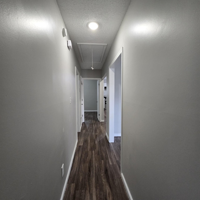 hall featuring attic access, baseboards, dark wood-type flooring, and a textured ceiling