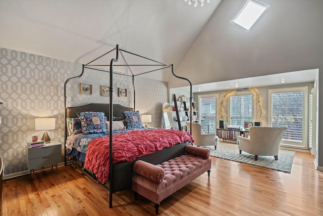 bedroom with high vaulted ceiling, multiple windows, wallpapered walls, and wood finished floors