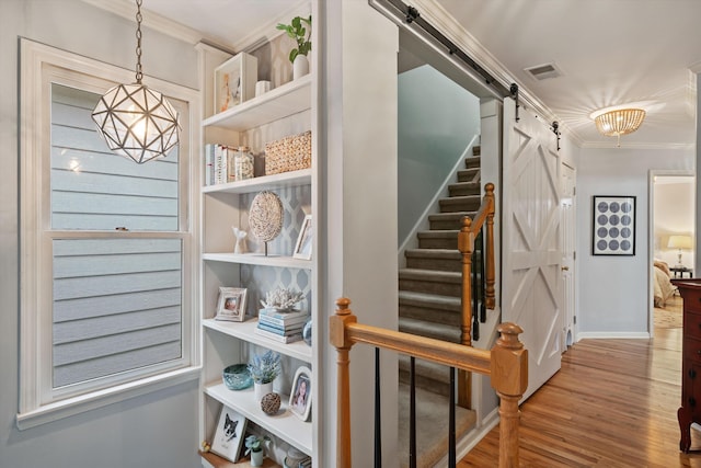 interior space featuring visible vents, ornamental molding, wood finished floors, a barn door, and an inviting chandelier