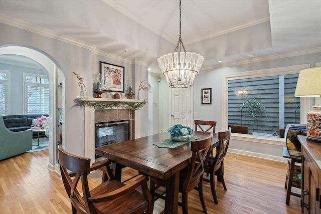 dining room featuring arched walkways, ornamental molding, a tile fireplace, and wood finished floors