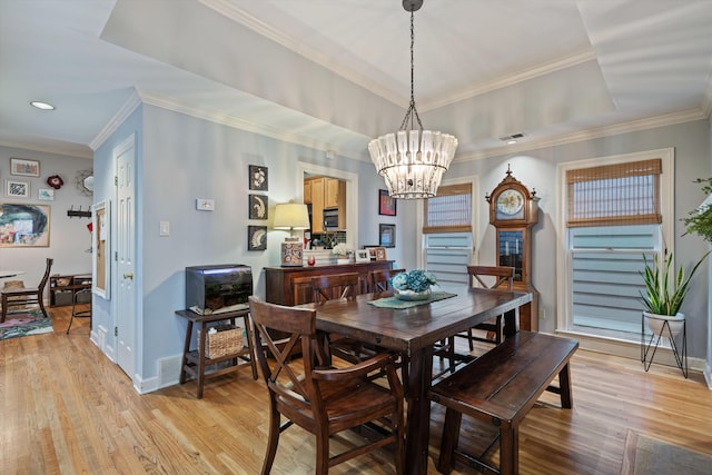 dining space featuring a raised ceiling, light wood-style flooring, ornamental molding, and a chandelier