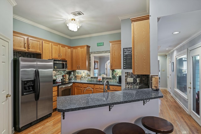 kitchen with a peninsula, stainless steel appliances, light wood-style floors, and ornamental molding