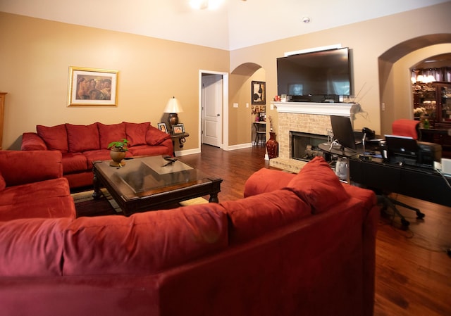 living area with arched walkways, a fireplace, baseboards, and wood finished floors