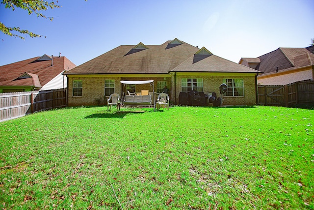 rear view of property with brick siding, a fenced backyard, and a yard