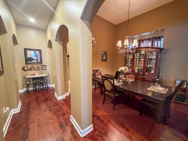 dining area with arched walkways, a notable chandelier, dark wood finished floors, and baseboards