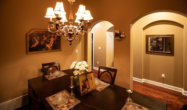 dining room with baseboards, arched walkways, a notable chandelier, and wood finished floors