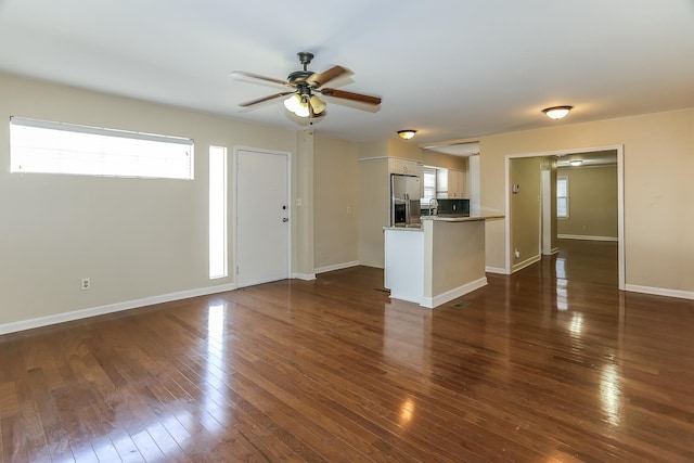 unfurnished living room featuring baseboards, a healthy amount of sunlight, dark wood-style floors, and a ceiling fan