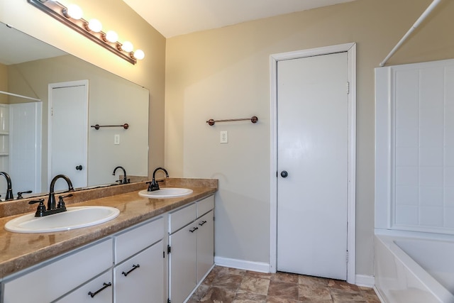 bathroom with double vanity, stone finish flooring, baseboards, and a sink