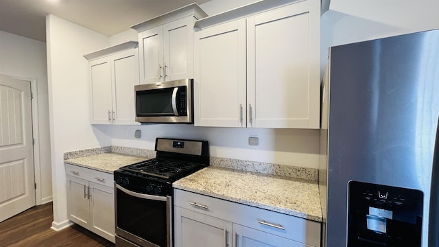 kitchen with white cabinetry, dark wood-type flooring, light stone counters, and stainless steel appliances