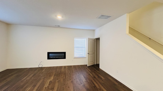 unfurnished living room with visible vents, baseboards, dark wood-type flooring, and a glass covered fireplace