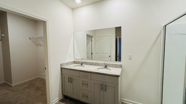 bathroom featuring a walk in closet, double vanity, baseboards, and a sink