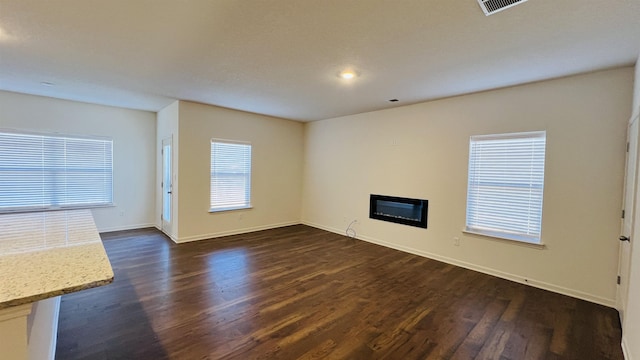 unfurnished living room with dark wood finished floors, a glass covered fireplace, and baseboards