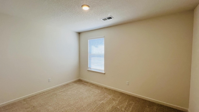 spare room featuring baseboards, light colored carpet, visible vents, and a textured ceiling