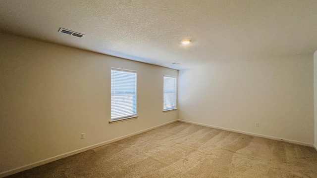 empty room with visible vents, baseboards, light colored carpet, and a textured ceiling