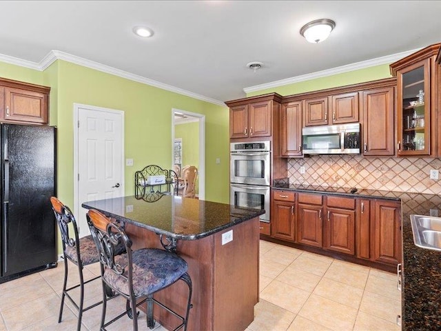 kitchen with light tile patterned floors, appliances with stainless steel finishes, a breakfast bar, and ornamental molding