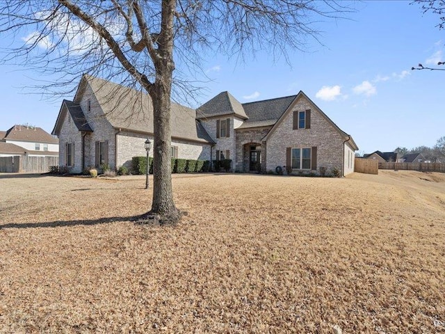 french provincial home featuring a front yard, fence, and stone siding